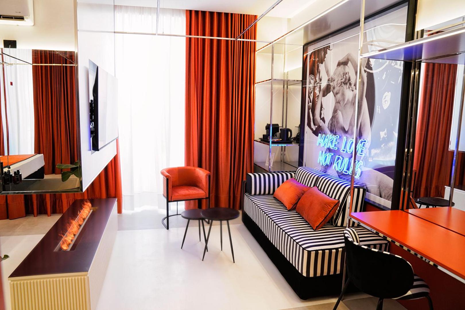 Soggiorno della suite con divano a righe, poltrona arancio, camino al bioetanolo e insegna al neon Make Love Not Rules
