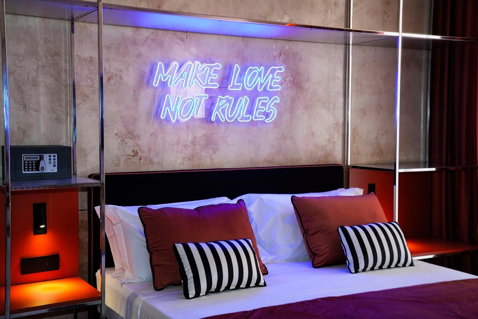 Letto matrimoniale con insegna al neon blu Make Love Not Rules e cuscini a righe