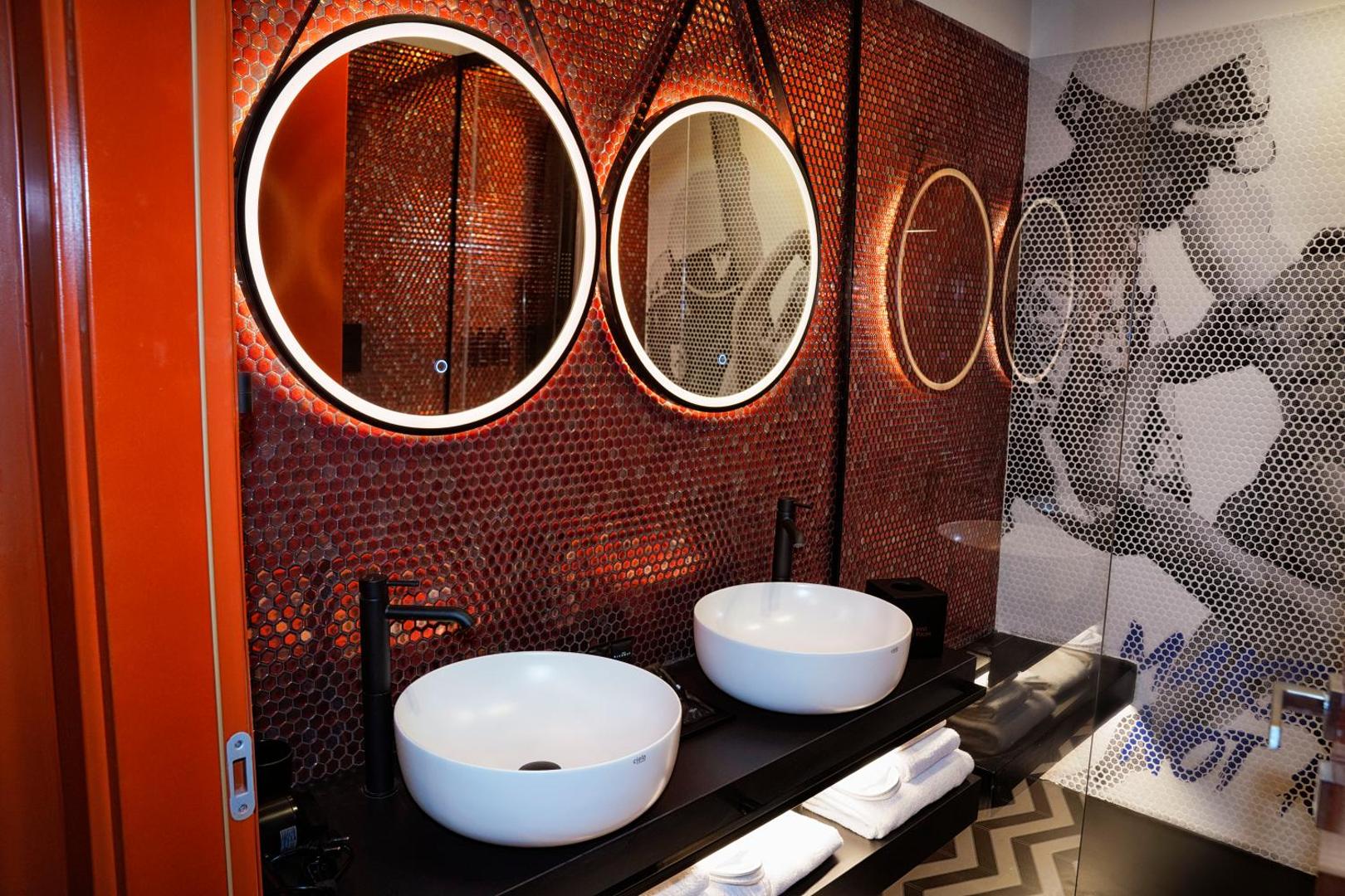 Bagno con doppio lavabo e specchi tondi retroilluminati su mosaico a nido d'ape arancio