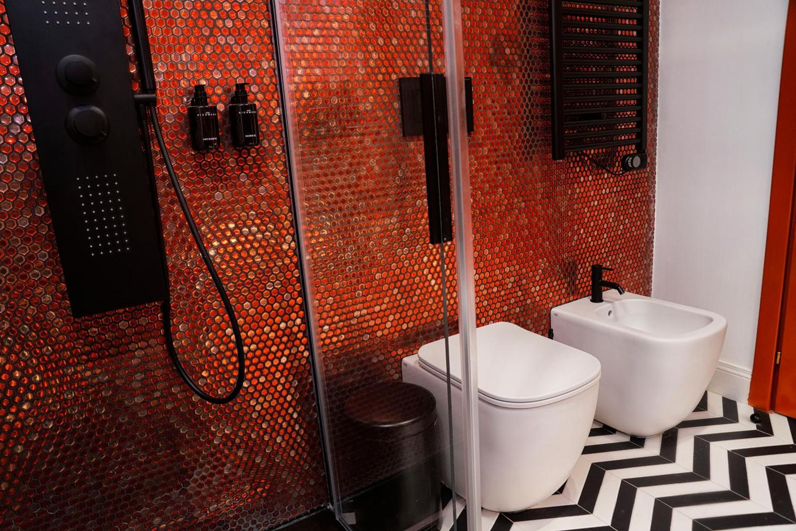 Doccia con pannello idromassaggio nero, wc e bidet su mosaico rosso e pavimento a chevron