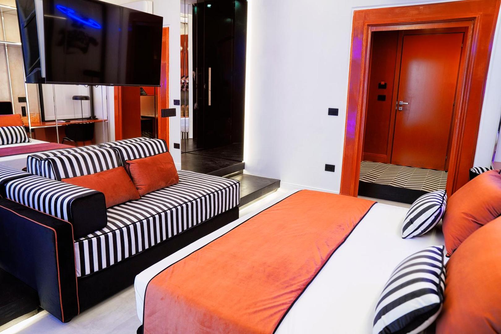 Zona notte con divano a righe, cuscini arancio, TV e porta d'ingresso della suite Saturno Contro
