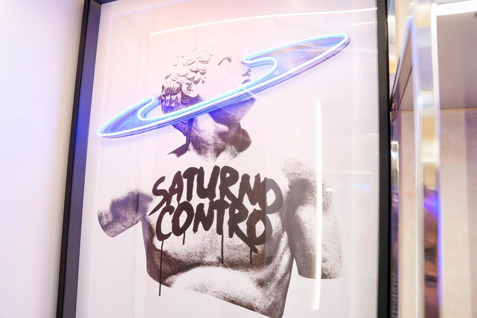 Opera incorniciata con statua e anello di Saturno al neon, scritta Saturno Contro