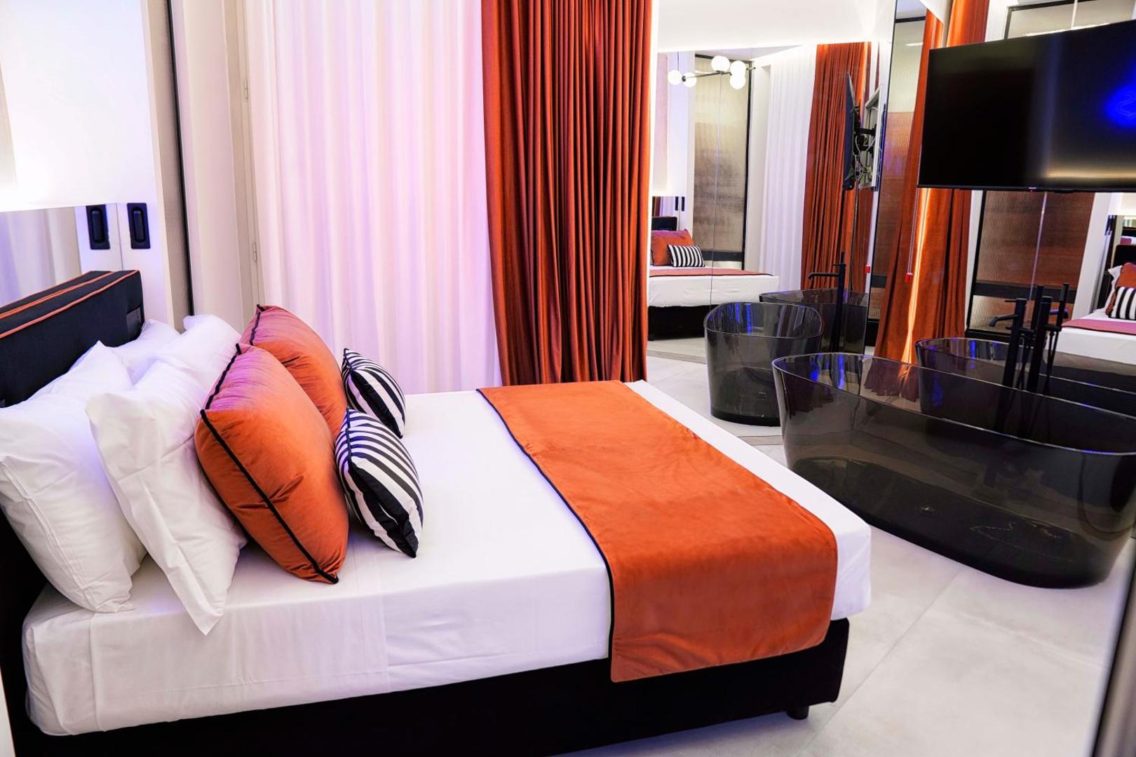 Lato del letto con plaid arancio e vasca freestanding trasparente fumé