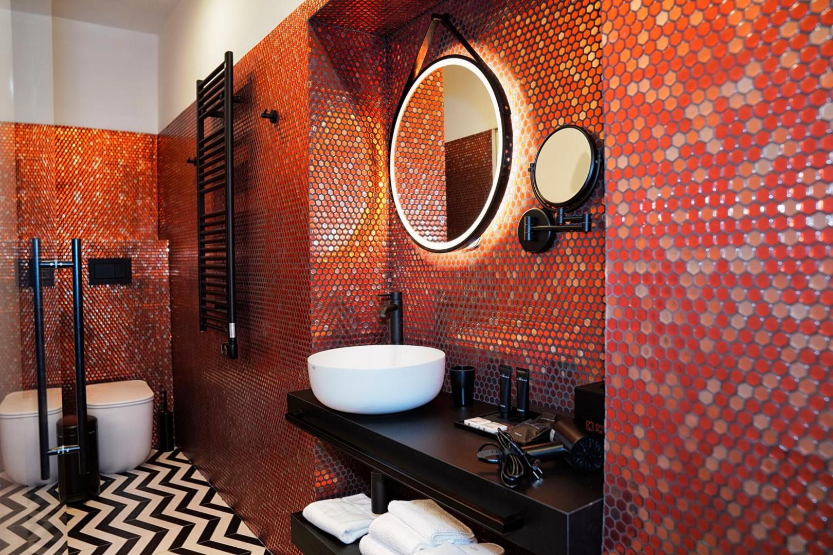 Bagno con mosaico rosso, specchio tondo retroilluminato, lavabo e wc