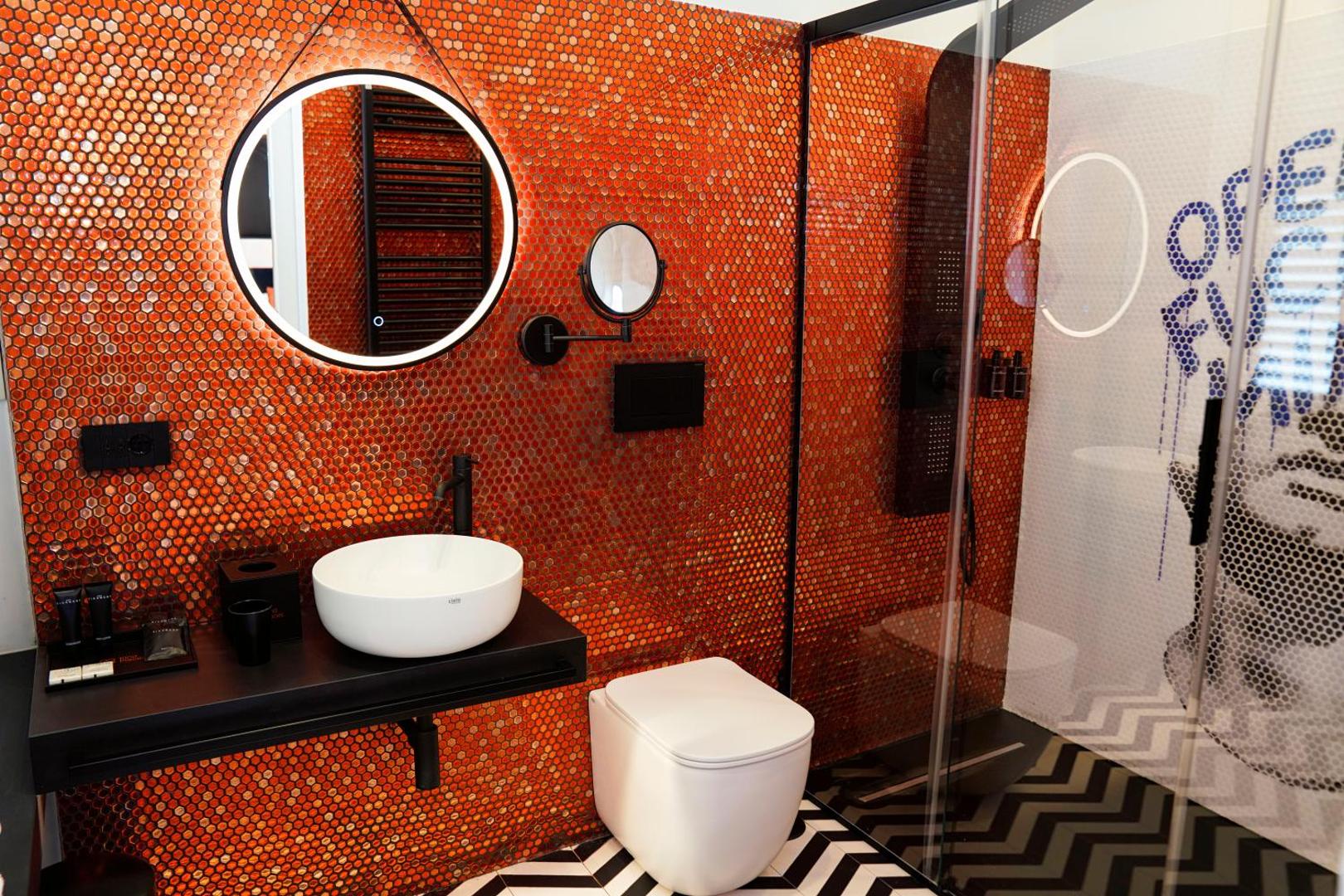 Bagno con mosaico arancio, specchio tondo, wc e doccia con murale Where Is My Mind